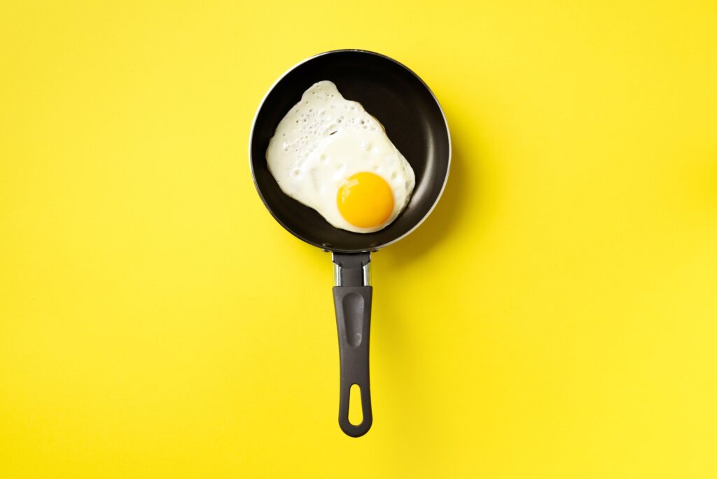 Creative food concept with fried egg on pan over yellow background. Top view. Creative pattern in